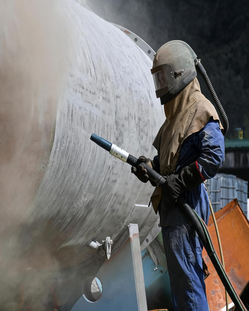 Industrial sandblasting professional working on large steel tank surface